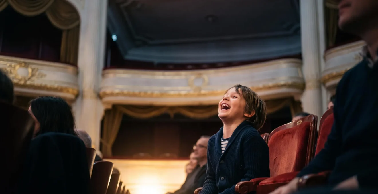 Jeune enfant riant aux éclats dans un fauteuil de théâtre français, entouré du public dans une salle chaleureusement éclairée
