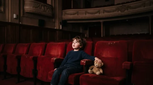 Jeune enfant emerveille assis dans un fauteuil de cinema, regardant vers un ecran hors champ, dans une salle obscure a l'ambiance chaleureuse
